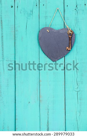 Blank slate heart with bronze skeleton key hanging from rope on rustic antique teal blue wooden background