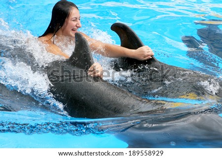 Beautiful young happy girl laughs and swims with dolphins in the blue dolphin pool lesson