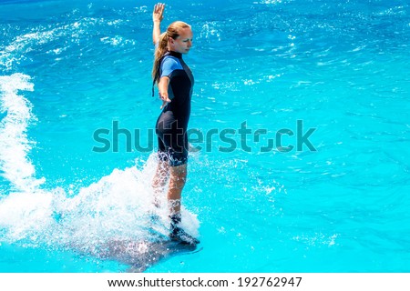 A young girl trains Glad beautiful dolphin in blue water in the pool on a bright sunny day on the original submission for tourists