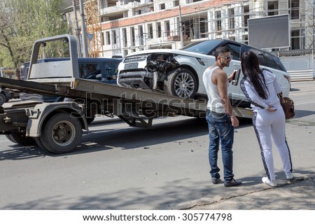 Odessa, Ukraine - May 3, 2015: A car accident in the city center. expensive car was loaded onto a tow truck after a car accident. The driver and passenger sad look at the work truck.