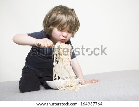 young boy eating his pasta on the couch