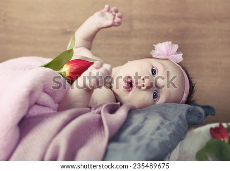 Baby covered with pink blanket and a flower in bed