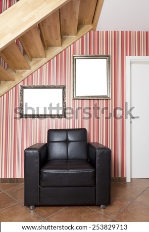 in a hallway with stairs is a leather armchair and empty frames hanging on the wall