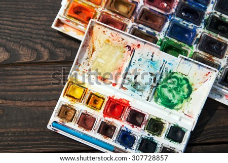 palette of watercolor paints in a dark wood. big and small box of multi-colored paints
