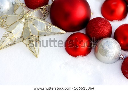 Red and Silver Christmas Ornament Bulbs and a star are framing the top corner of white, freshly fallen snow background, with room for text, copyspace.  Could be used as Christmas greeting card.