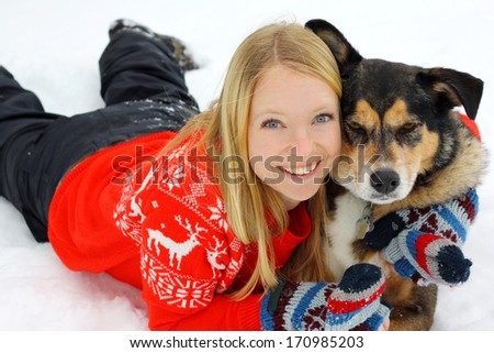 a young woman in her thirties is laying outside in the winter snow with her German Shepherd mix dog, hugging him.