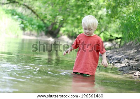 A cute young child is playing outside, swimming in the river in the woods on a summer day.