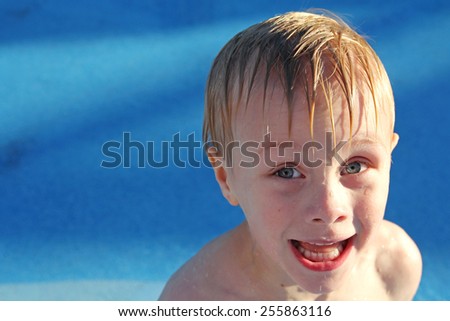 A young child is making a funny face because he is cold while playing outside in the swimming pool.