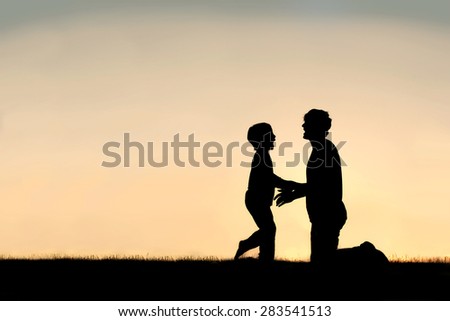 Silhouette of a happy little child greeting his father to hug him outside on a summer day, silhouetted against the sunset in the sky.