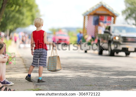 A young boy child standing outside in the summer watching a small town american parade and holding a candy bag.