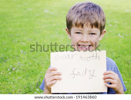 Cute young boy with a missing tooth holding a sign for the tooth fairy