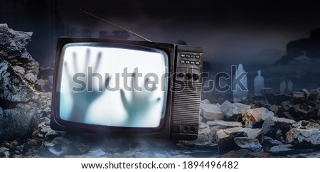 Horror photo of an old black  scary haunted tv set with ghost hands on screen, standing on dark foggy ruined city with spirit figures background.