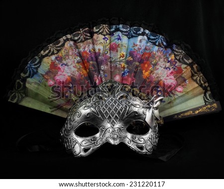 Mask with fan.Silver carnival mask laying with folding fan on black fabric background.