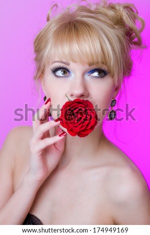 Portrait of beautiful young woman with red lipstick, nails and holding red rose in hands, on pink background, valentines day