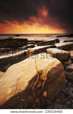 The sun sets on the beautiful Dorset coastline illuminating glistening rocks with orange and yellow highlights