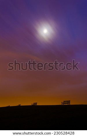 Light pollution produces an orange glow above lonely, empty benches on a hilltop near Weymouth