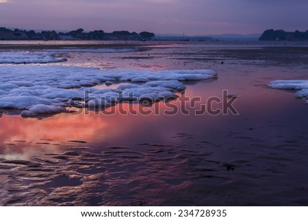 Rare snowfall on Poole Harbour beach with red sky reflected in the wet sand