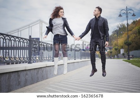 Couple in leather jackets jumping on seafront on a cloudy day outdoors