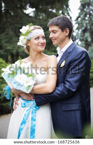 Young couple hugging in wedding gown. Bride holding bouquet with white lilies