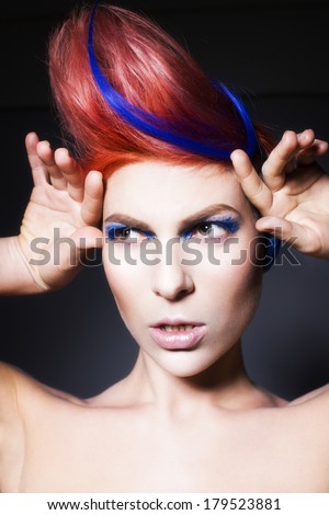 Young person with blue eye shadows, blue ears and pink hair with blue strand on it looking sideways. Black background