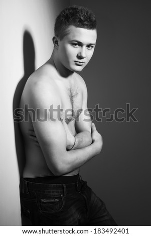 Shirtless handsome man with fit body lean against a wall indoor. Black and White