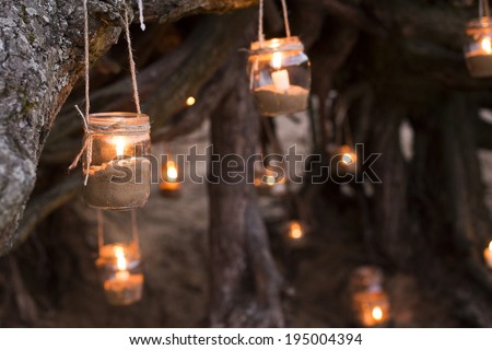 Beautiful decorated romantic place for a date with jars full of candles hanging on tree and standing on a sand. Copy Space