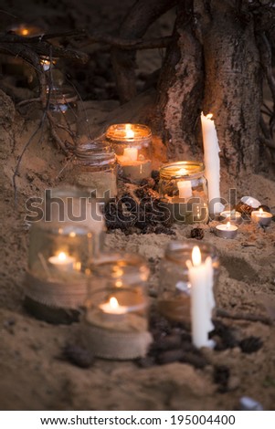 Beautiful decorated romantic place for a date with jars full of candles hanging on tree and standing on a sand