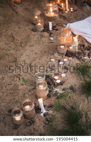 Beautiful decorated romantic place for a date with jars full of candles hanging on tree and standing on a sand