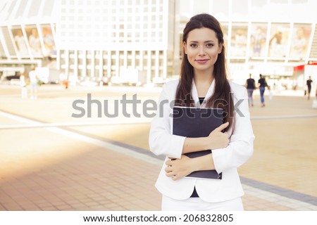 Beautiful brunette business woman in white suit with folder of documents in her hands outdoors. copy space