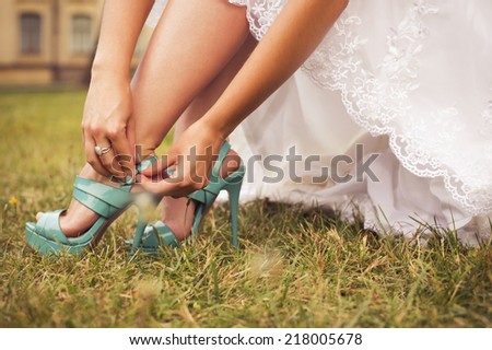 Beautiful bride preparing to get married in white dress and fasten her tiffany blue shoes on the grass in the park alone. outdoors. copy space