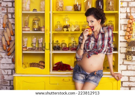 Beautiful brunette woman on a 7th month pregnancy in plaid shirt and jeans shorts on a yellow kitchen. pin up style. copy space