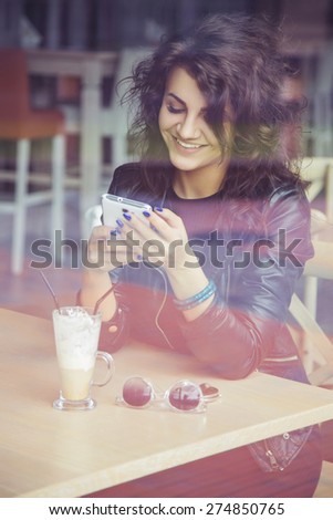 Brunette beautiful stylish caucasian woman in casual outfit on a walk on european city street sitting at the cafe typing message on her phone
