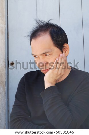 outdoor portrait of a young asiatic man thinking  and looking ahead against an antic blue door for background