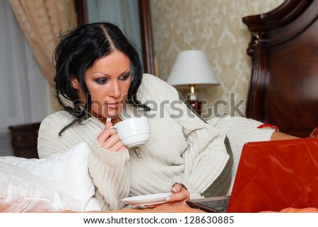 Young woman with laptop lies on the house bed.