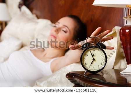 Young sleeping woman and alarm clock in the bedroom.  Selective focus on a alarm clock.