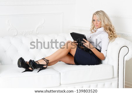 Young business woman with computer tablet sits on the white sofa.