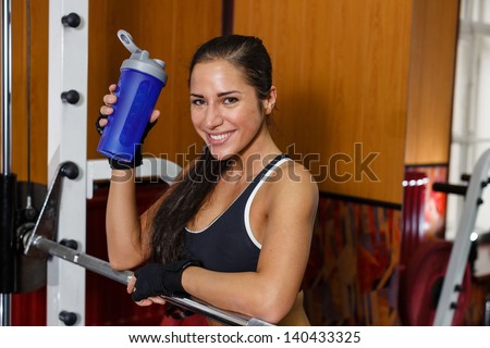 The sports young woman with a protein cocktail in a shaker stands in a gym. Sports nutrition.