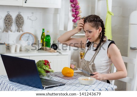Beautiful woman in an apron with notebook cooks in the kitchen.