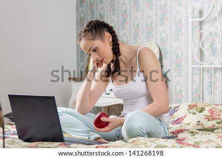 Young woman with laptop sits on the house bed in the bedroom.