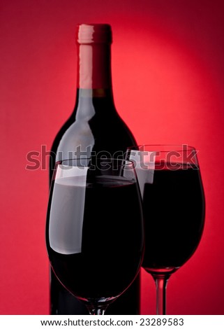 Bottle of a red vintage wine and two glasses on a red background