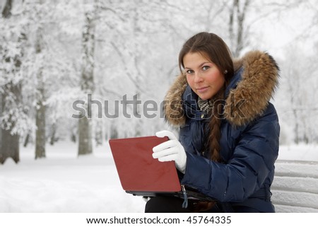 The beautiful girl with the laptop sits on a bench in winter park.
