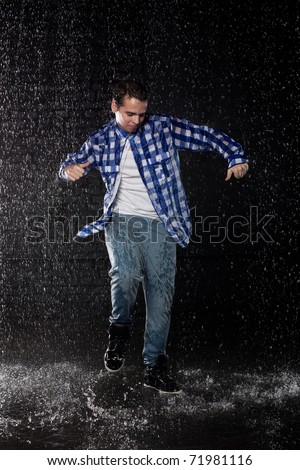 Young man dancing in water under rain on a black background.  Modern dances.