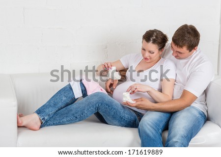 Happy pregnant family  with children\'s clothes sit on the sofa in the room.