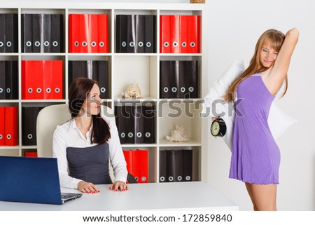 Sleepy woman in a nightgown with alarm clock in a hand stands in the office of the the chief. Being late for work.