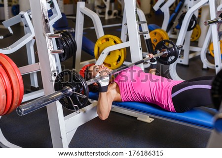 Sports young woman doing exercises with barbell on bench in the gym.  Bar Bench Press.