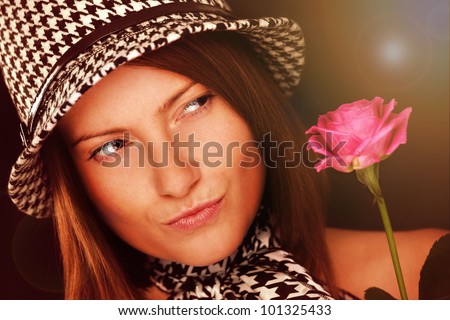 A picture of a beautiful woman looking at a pink rose against dark background