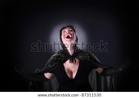A portrait of a hooded female vampire standing against black background