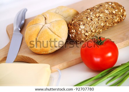 A picture of breakfast rolls butter and tomato on a wooden board