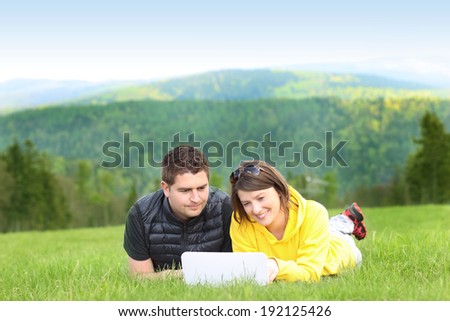 A picture of a young couple and laptop on the grass in the mountains
