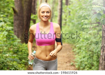 A picture of a woman jogging in the forest with a bottle of water